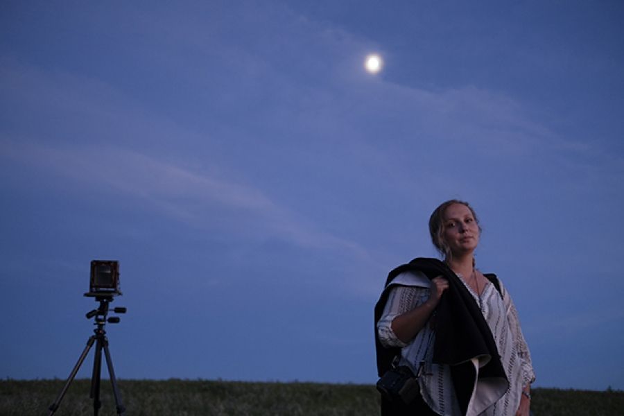 A woman is standing in a field with a camera on a tripod.