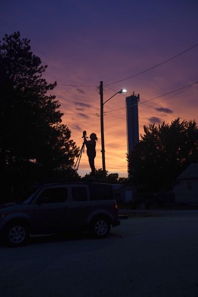 A man is standing on top of a street light at sunset.