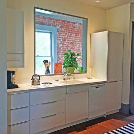 Modern kitchen with white cabinets and a window revealing a brick wall.