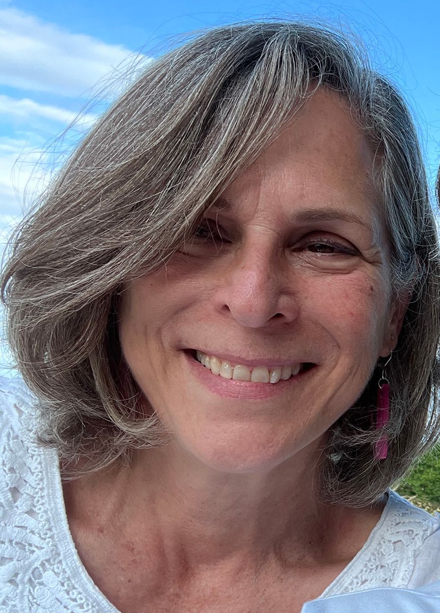 Woman with gray hair smiles, blue sky background.