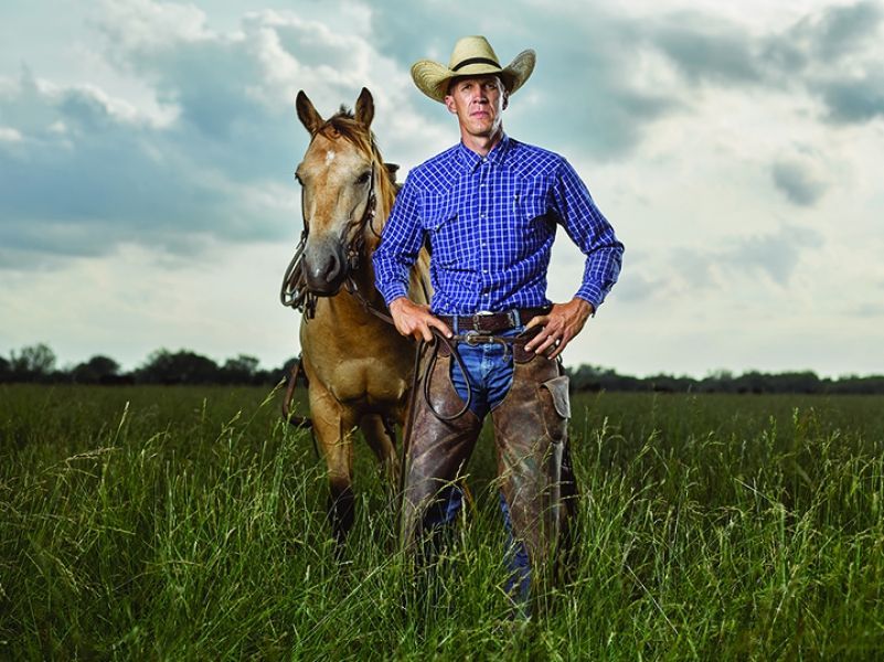 A man in a cowboy hat is standing next to a horse in a field.