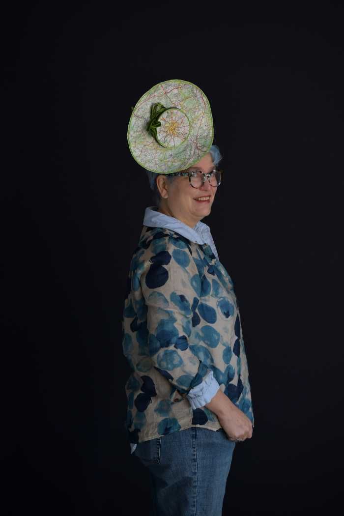 A woman wearing a hat with a flower on it is standing in front of a black background.