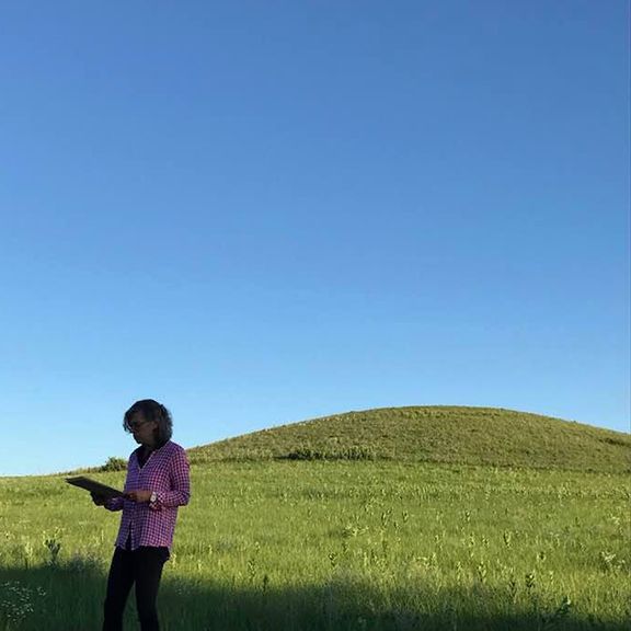 A woman is standing in a grassy field holding a book.