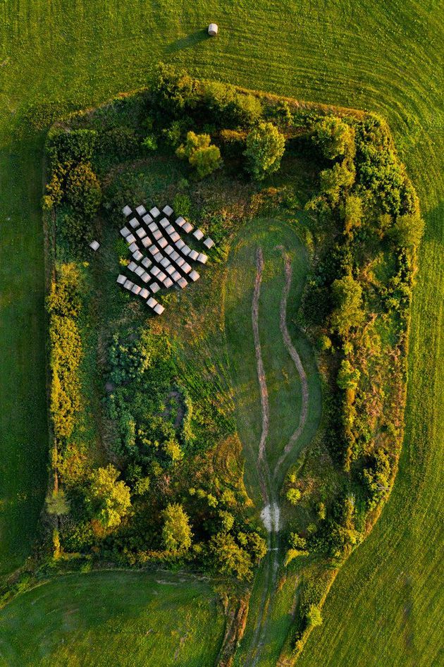 Aerial photo of a rectangle of ground that once held a missile silo. Green trees edge the rectangle of green grass, with hay bales stored in one corner.