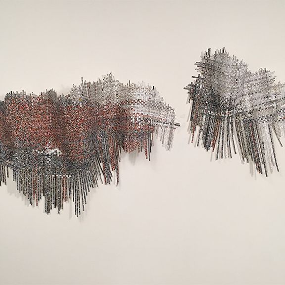 Abstract metal artwork on a white wall. Two textured, rectangular shapes, one reddish, the other gray.