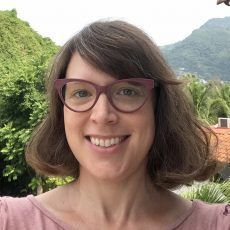 A woman wearing glasses and a pink shirt is smiling for the camera.