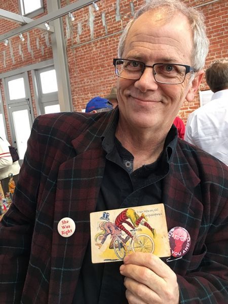 A man wearing glasses and a plaid jacket is holding a card