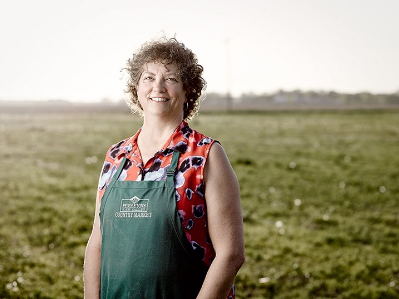 A woman in an apron is standing in a grassy field.