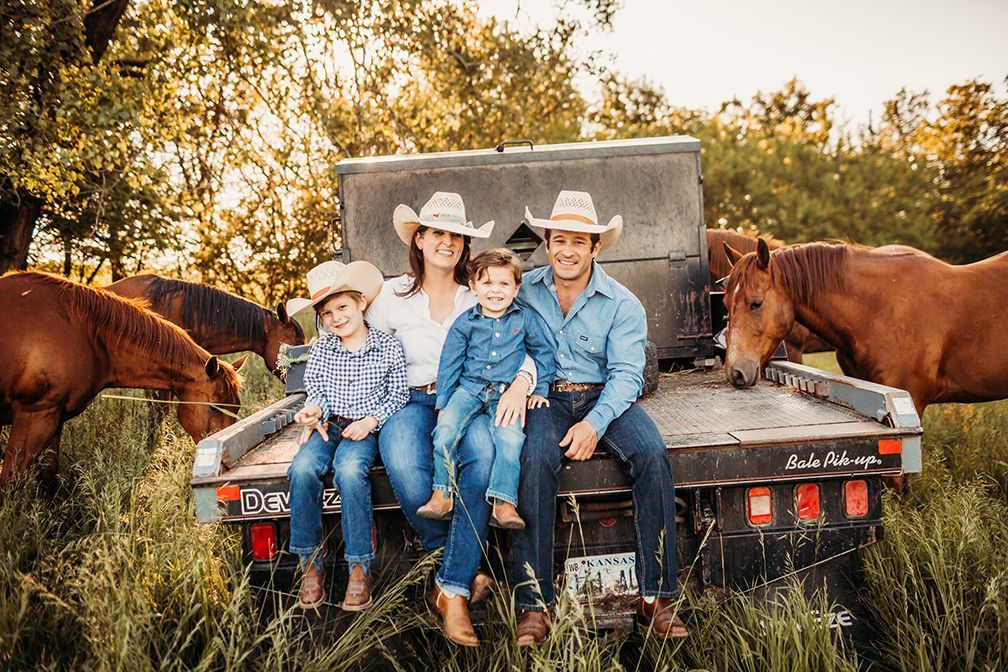 A family is sitting on the back of a truck with horses.