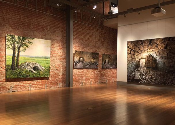 A room with a wooden floor and a brick wall with paintings on the wall.