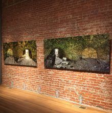 Three paintings are hanging on a brick wall in a museum.