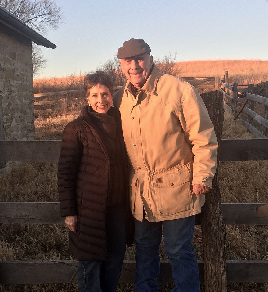 A man and a woman are posing for a picture in front of a wooden fence