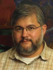 Man with glasses and beard, wearing a plaid shirt, looking directly at the camera.
