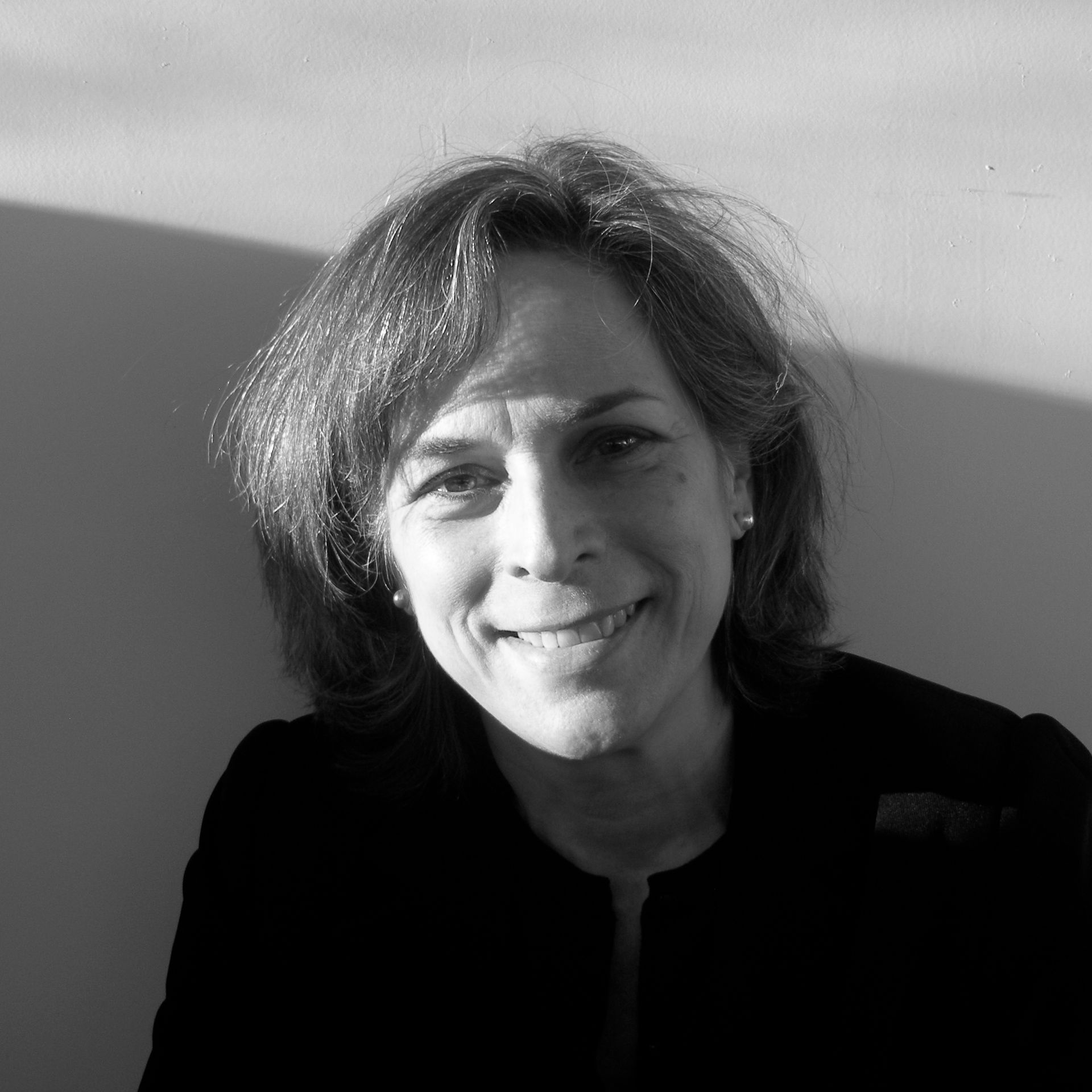 A woman in a black jacket is smiling in a black and white photo.