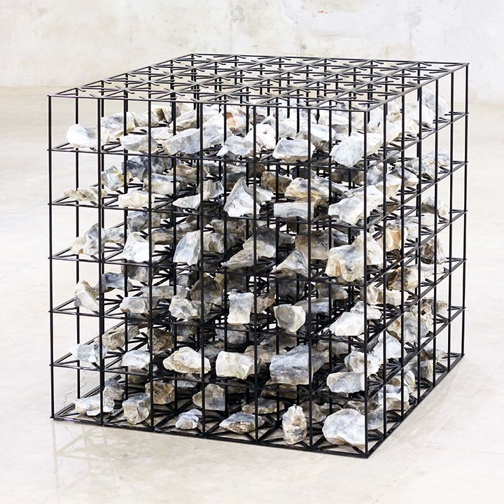 Black metal cube filled with gray rocks on a light marble floor.