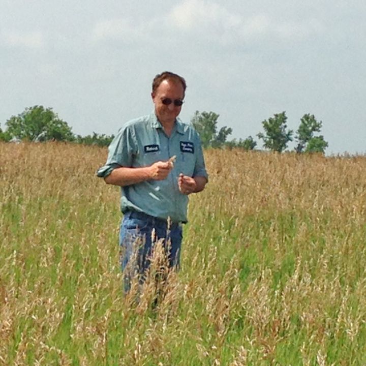 A man standing in a field of tall grass with a name tag that says ' smith ' on it