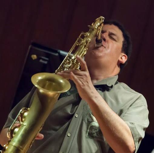 Man playing a golden saxophone, indoors, wearing a light green shirt; performing with eyes closed.