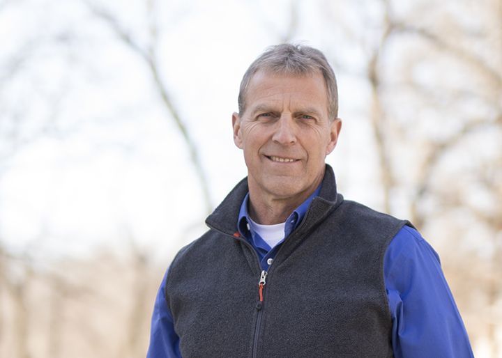 A man wearing a vest and a blue shirt is smiling for the camera.