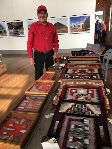 A man in a red shirt stands in front of a table full of native american artifacts