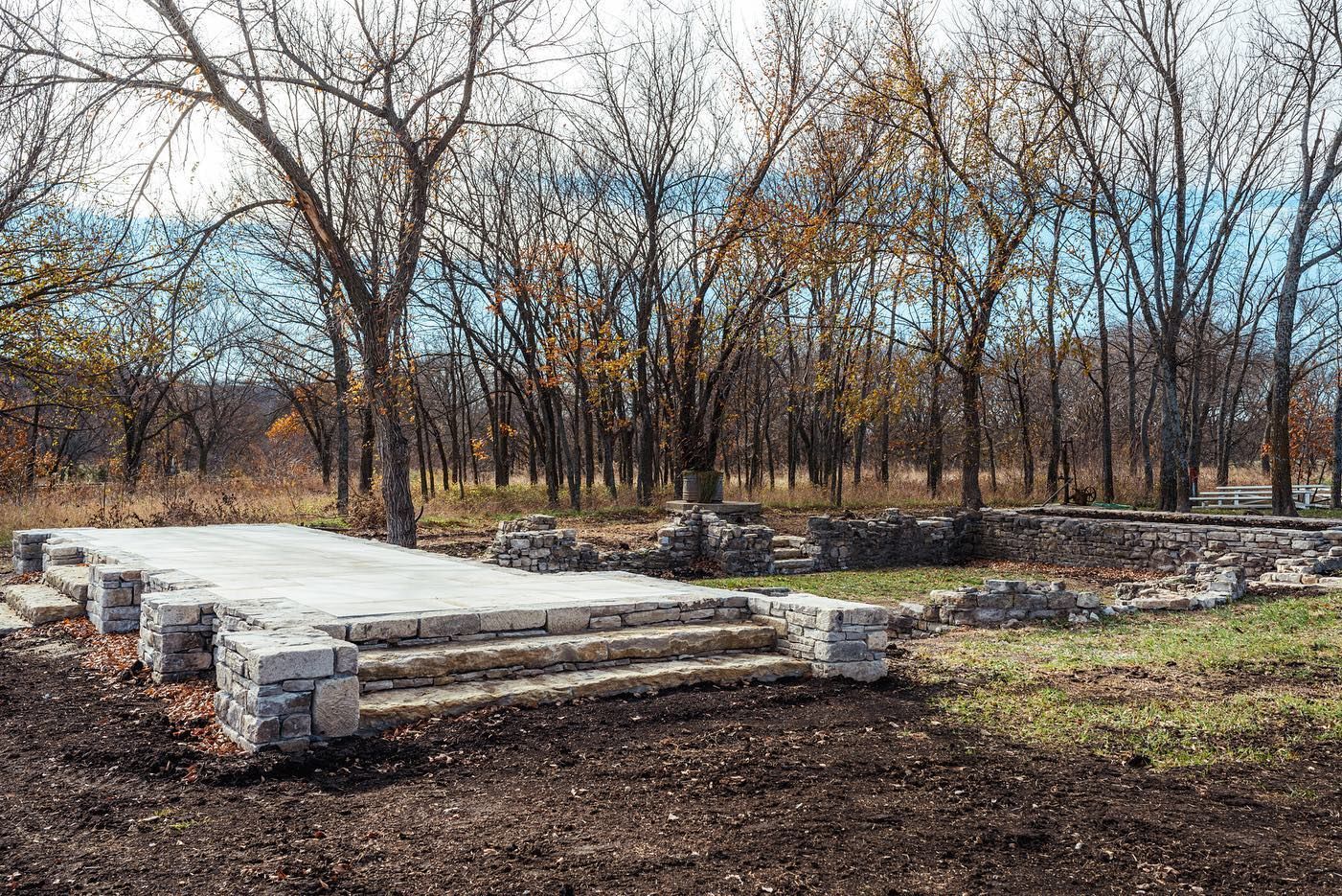 Stone foundation and steps in front of a grove of trees with fall foliage.