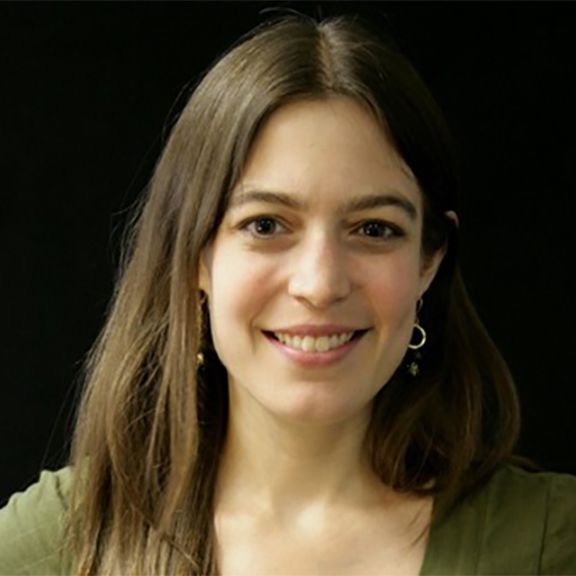 A woman wearing a green shirt and earrings smiles for the camera