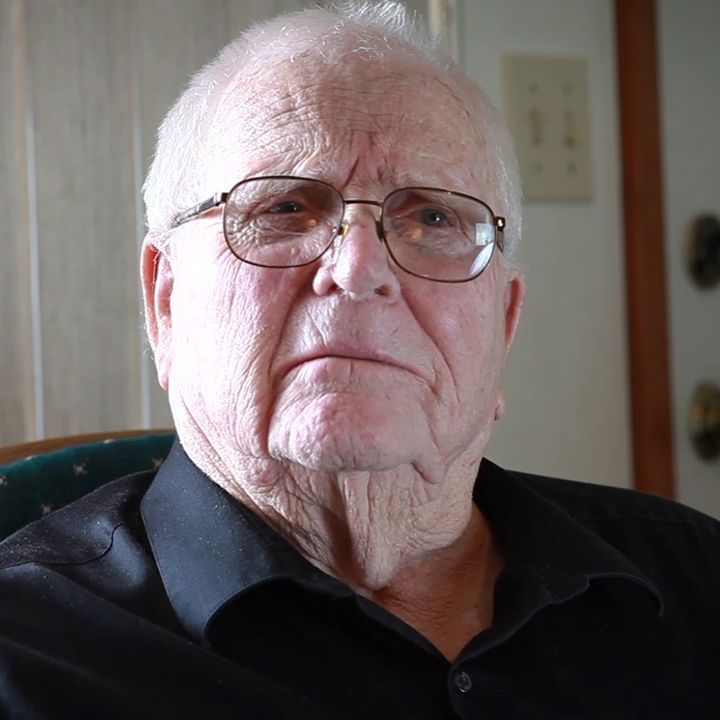 Elderly man with glasses and a black shirt looking directly at the camera.