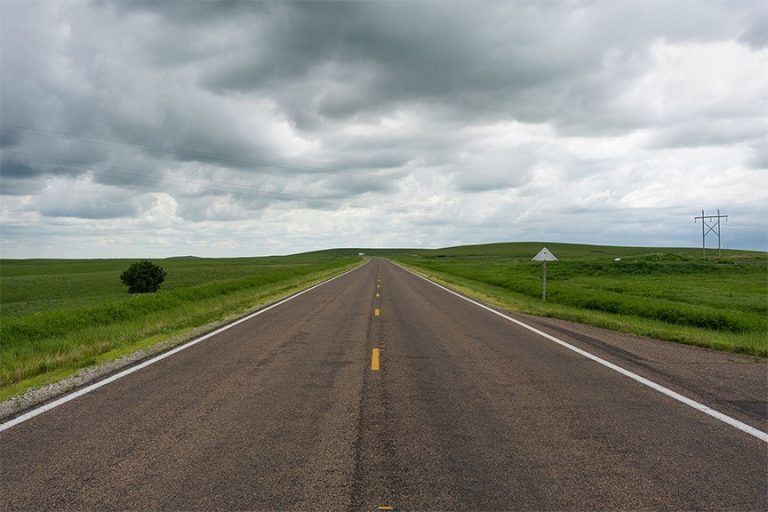 An empty highway going through a grassy field on a cloudy day
