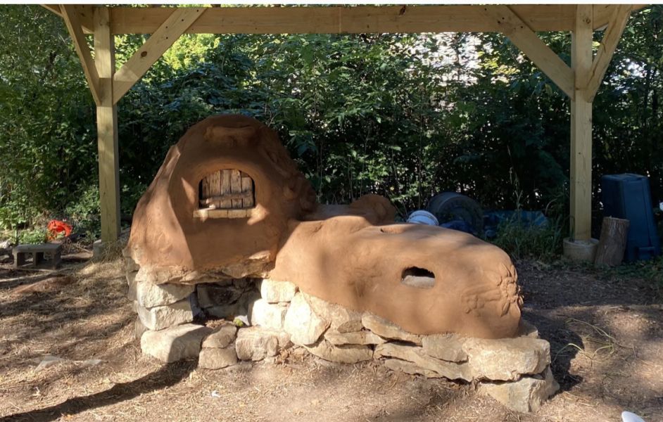 Mud oven with wooden frame. Brown clay construction on a stone base, outdoors.