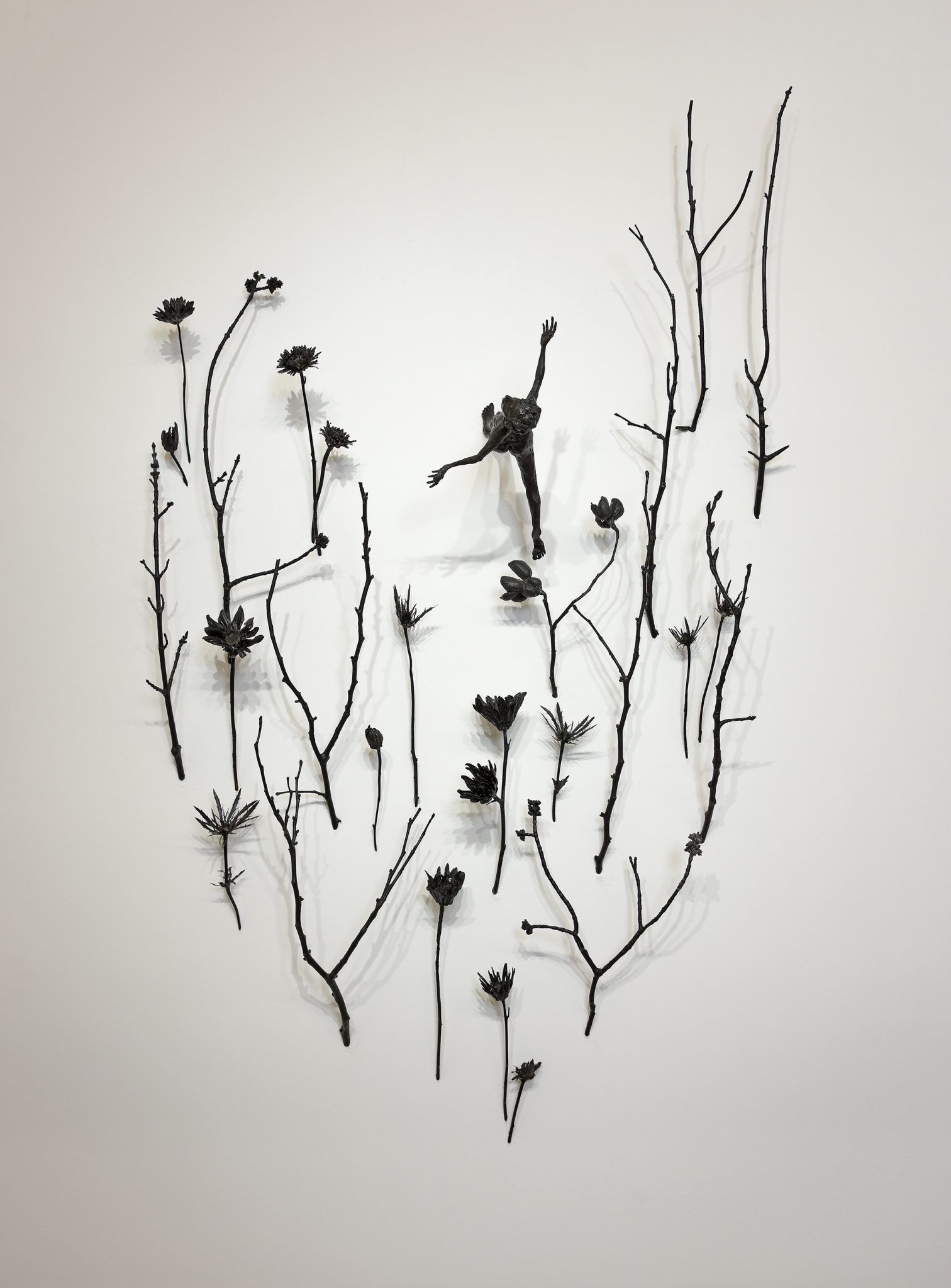 Metal sculpture: a dancing figure surrounded by abstract branches and flowers on a white wall.