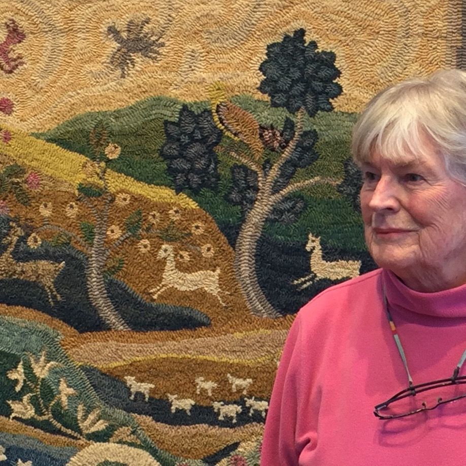 A woman wearing glasses stands in front of a painting