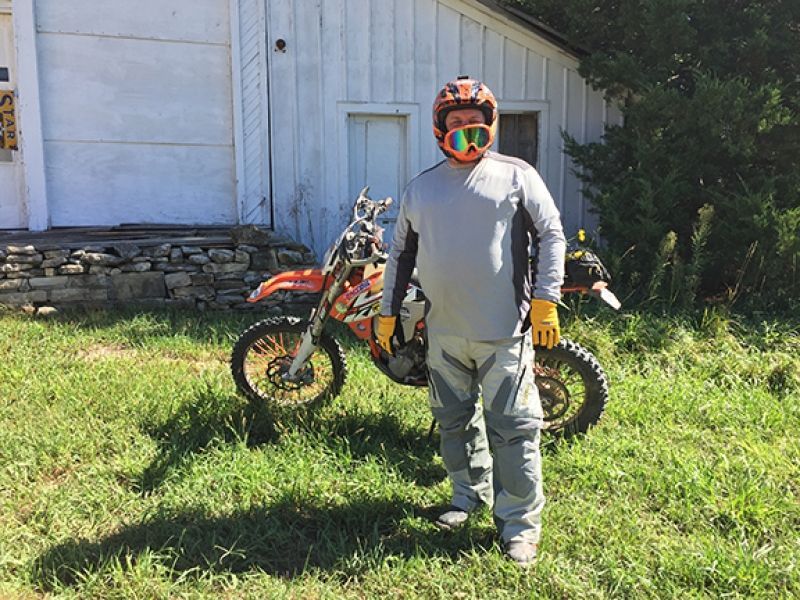 A man wearing a helmet and goggles is standing in front of a dirt bike.