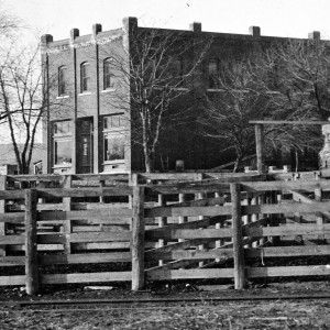Brick building with wooden fence in front, bare trees; outdoors.