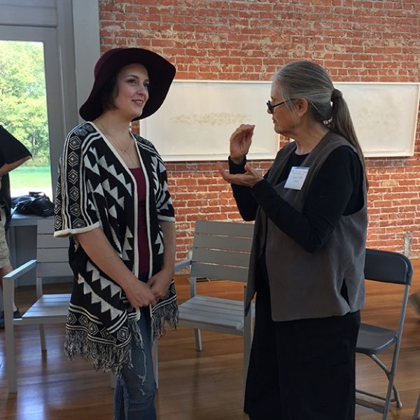 Two women are talking in front of a brick wall