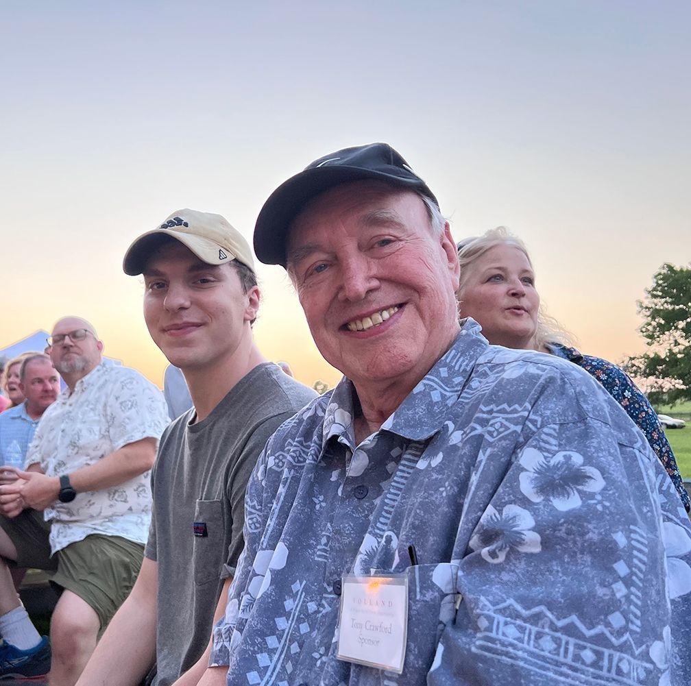 Smiling man in a floral shirt, young man, and group outdoors at dusk.
