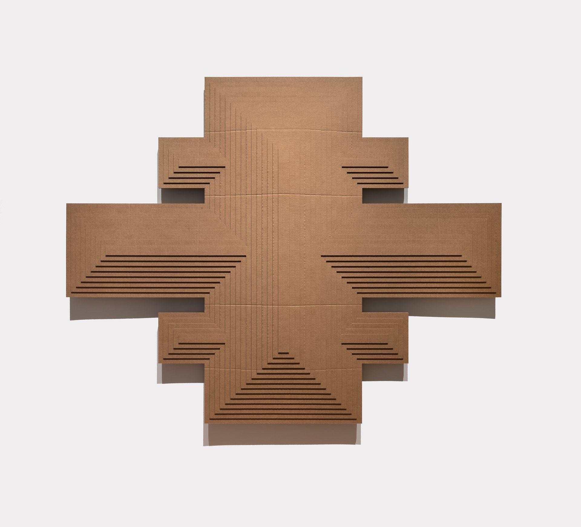 Brown, cross-shaped geometric sculpture with layered steps, horizontal slits, against a light background.