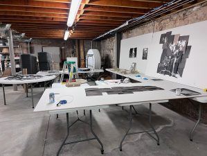 Workshop: Tables with materials and photos are in a basement with exposed beams.