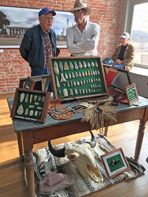 Three men are standing around a table with a display of native american artifacts.