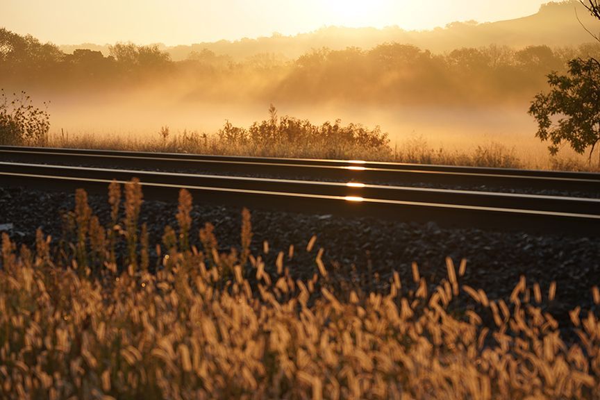 The sun is shining through the fog over the train tracks.