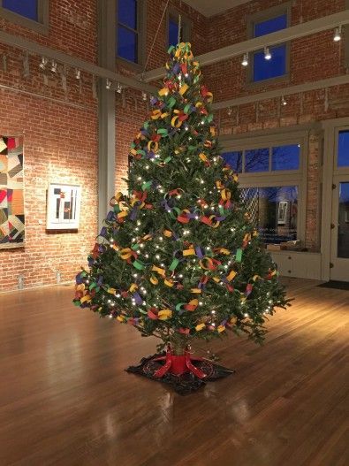 Christmas tree decorated in an art gallery, with red brick walls and hardwood floors.