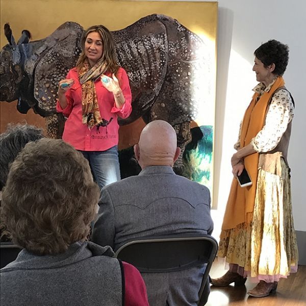 A woman in a pink shirt stands in front of a painting of a rhino