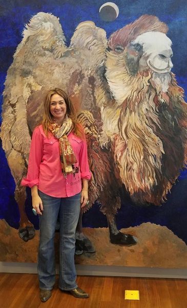 A woman is standing in front of a painting of a camel.