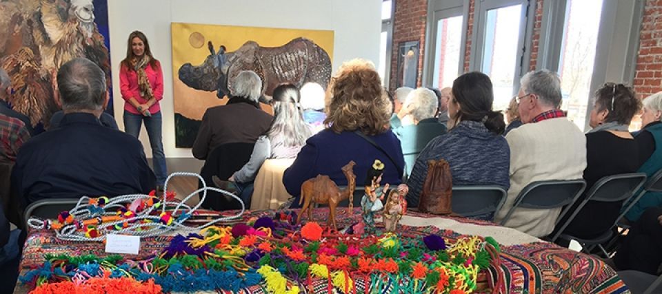 A group of people are sitting at a table in front of a painting.