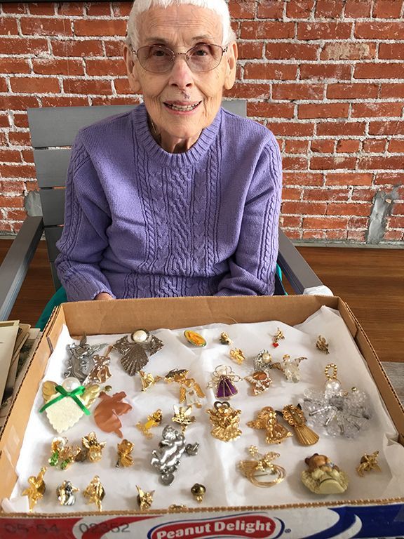 An elderly woman is sitting in a chair holding a box of peanut delight