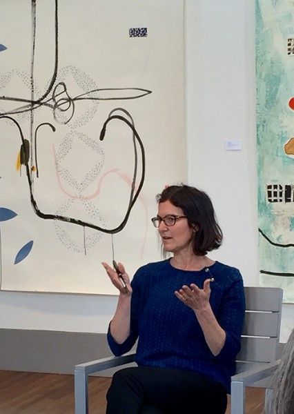 A woman in a blue shirt is sitting in front of a painting