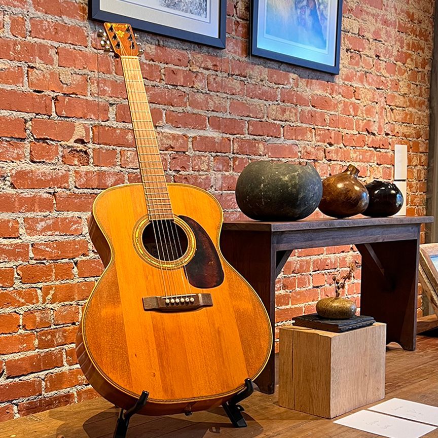 An acoustic guitar is on display in front of a brick wall