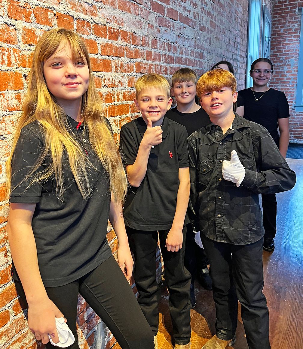 a group of 6th-8th grade students, dressed in black, smile at the camera with thumbs up before performing chimes with the adult bell choir