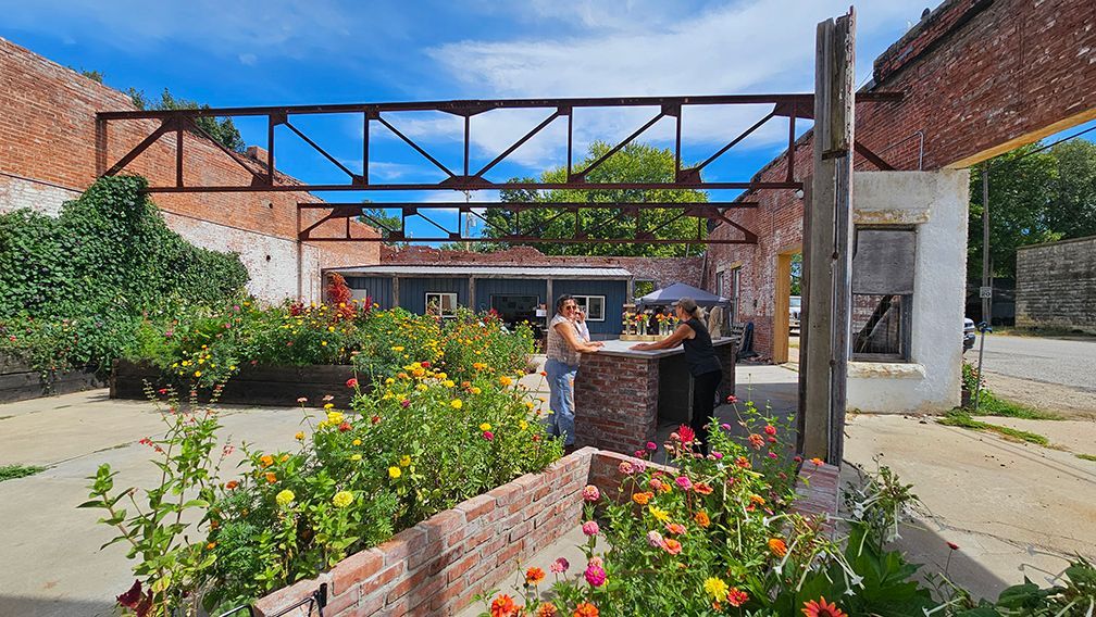 A woman is standing in front of a brick building surrounded by flowers.