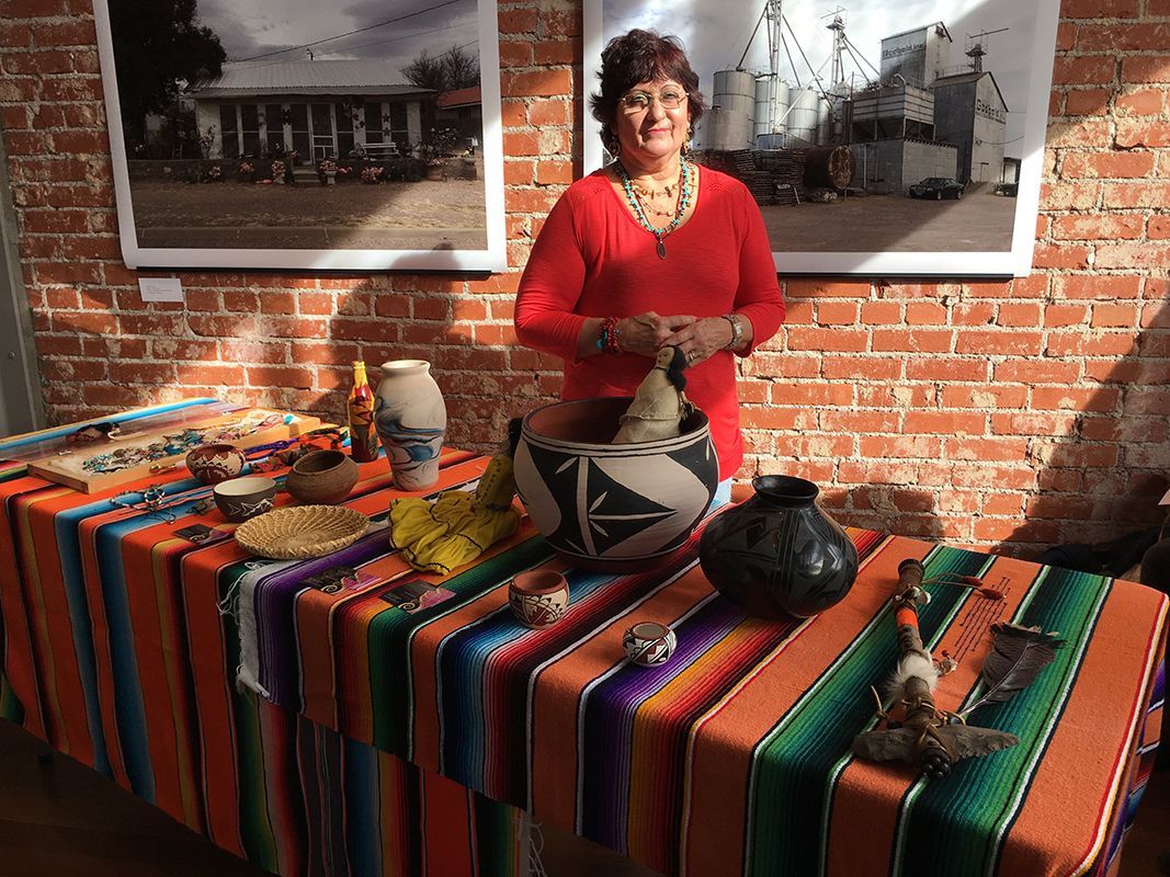 A woman is standing in front of a table with vases and blankets.