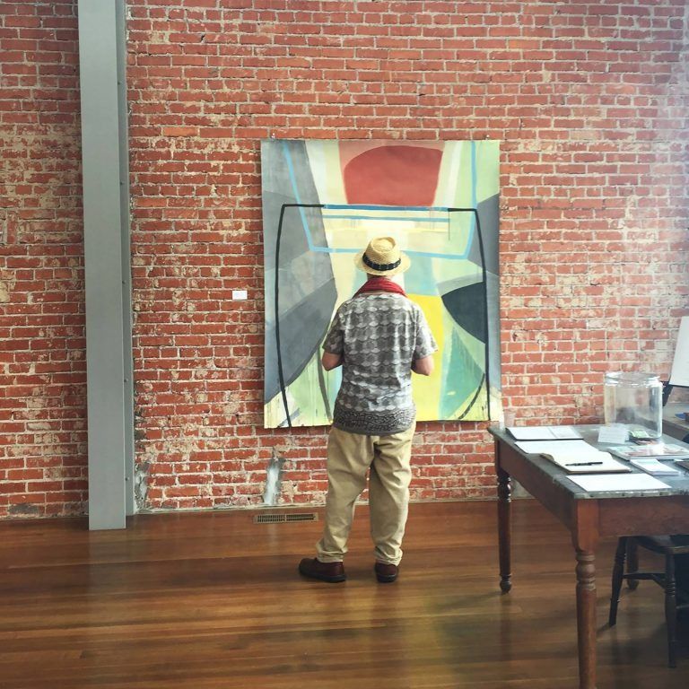 A man in a hat is looking at a painting on a brick wall