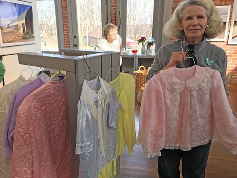 A woman is holding a pink shirt in front of a rack of clothes.